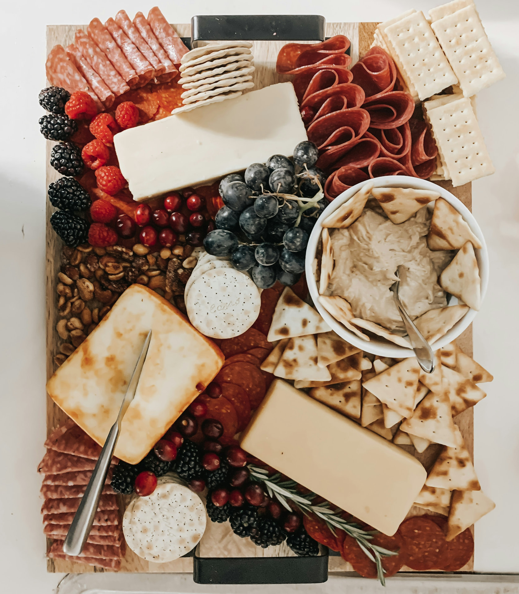 Overhead charcuterie board with cheeses, folded meats, berries, crackers and hummus
