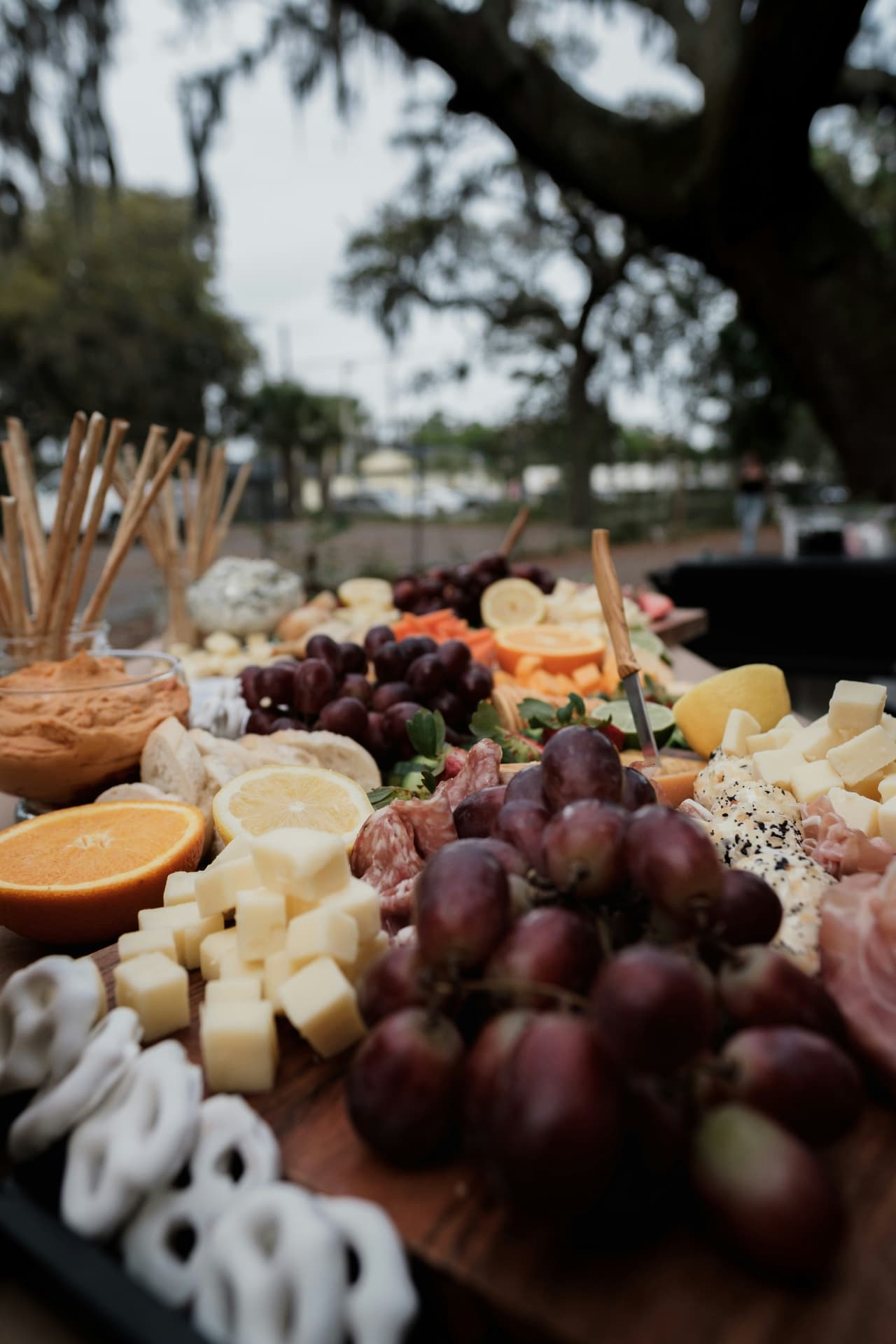 Outdoor charcuterie table with grapes, cheeses, citrus and cured meats