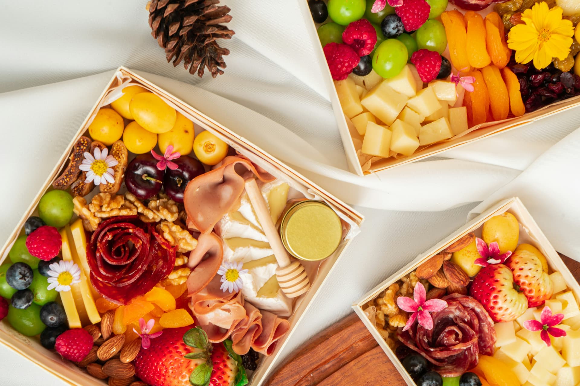 Colorful charcuterie gift boxes with cheese, fruit, nuts, flowers and honey