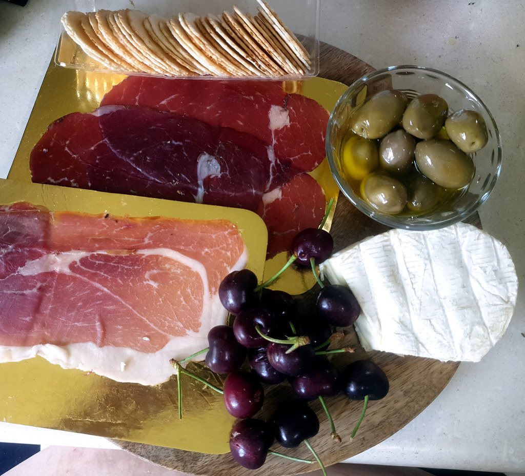 Holiday platter with cured meats, cheeses, crackers, olives and cherries